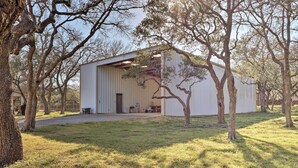 A spacious, single-story building with a large open garage door, surrounded by trees and a grassy lawn. - Georgetown Barn Studio on > 7 Acres: Pet Friendly! (Georgetown)