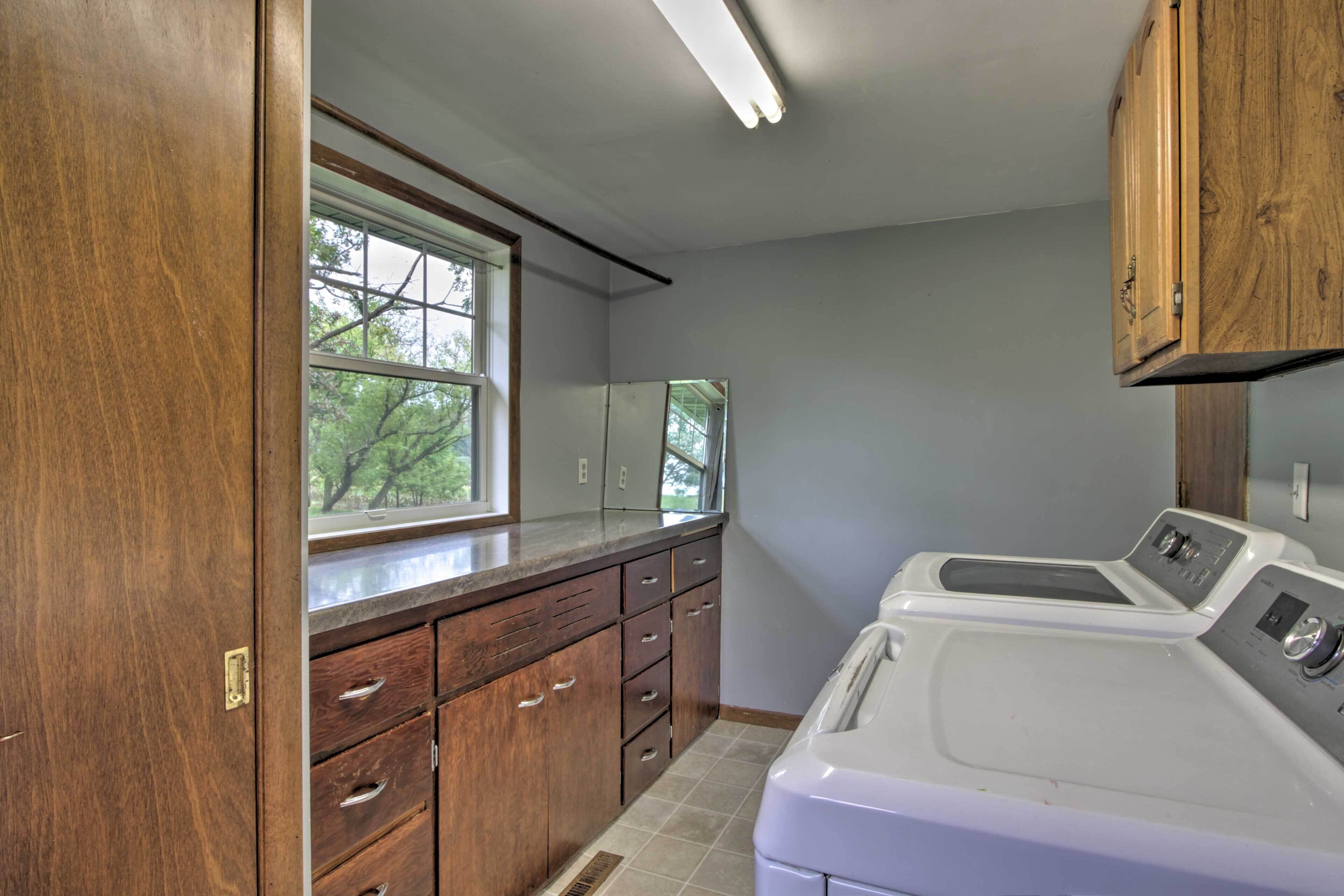 A laundry room with wooden cabinets, a large window, and a front-loading washing machine.
