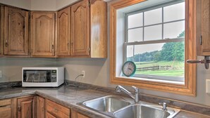 A kitchen with wooden cabinets, a stainless steel sink, a microwave, and a window with a view of greenery.