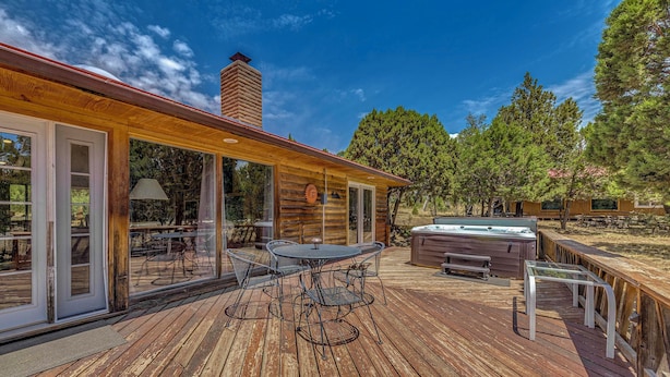 A wooden deck with a hot tub, outdoor seating, and a glass door leading to a patio area. - Hot Tub, Deck & Fireplace at Rustic Alto Cabin! (Alto)