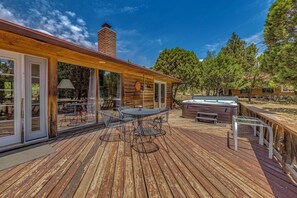 A wooden deck with a hot tub, outdoor seating, and a glass door leading to a patio area. - Hot Tub, Deck & Fireplace at Rustic Alto Cabin! (Alto)