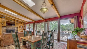 A cozy living room with a fireplace, wooden furniture, and large windows offering a view of the outdoors. - Hot Tub, Deck & Fireplace at Rustic Alto Cabin! (Alto)