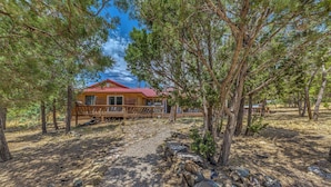 A wooden cabin with a red roof, surrounded by pine trees and a gravel path leading to it. - Hot Tub, Deck & Fireplace at Rustic Alto Cabin! (Alto)