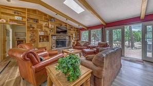 A spacious living room with leather furniture, a fireplace, and large windows offering a view of the outdoors. - Hot Tub, Deck & Fireplace at Rustic Alto Cabin! (Alto)
