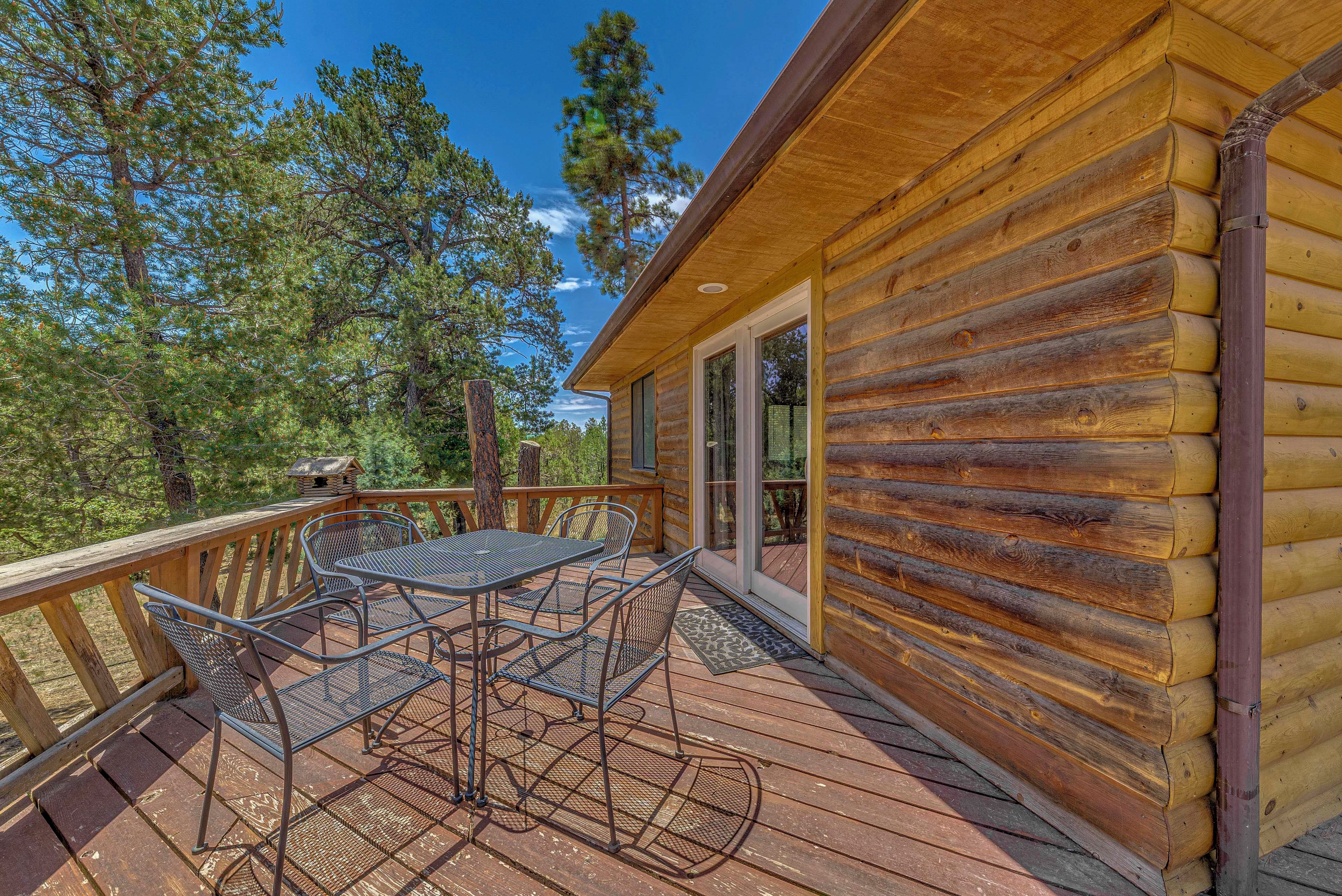 A wooden cabin with a deck, metal table and chairs, and a glass door leading to a covered area.