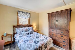 A bedroom with a wooden bed, a large wardrobe, a bedside table with a lamp, and a window with a patterned curtain. - Catskills Getaway w/ Hot Tub on 45 Acres! (Hannacroix)