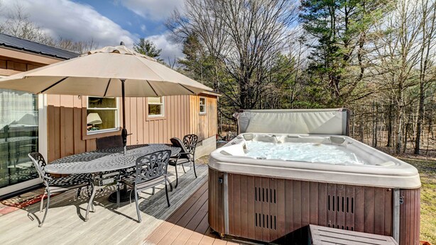 Une terrasse en bois avec des meubles d’extérieur, un jacuzzi et une pièce fermée par des baies vitrées.