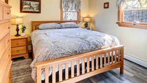 Une chambre à coucher avec un lit en bois, deux tables de chevet avec des lampes, une commode, une fenêtre avec des rideaux et un tableau accroché au mur.