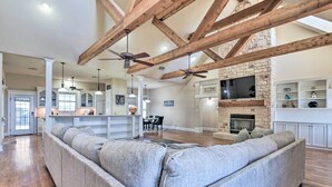 A spacious living area with a large gray sectional sofa, wooden beams on the ceiling, a stone fireplace, and a television mounted on the wall. - 8 Mi to White Rock Lake: Spacious Krum Home (Krum)