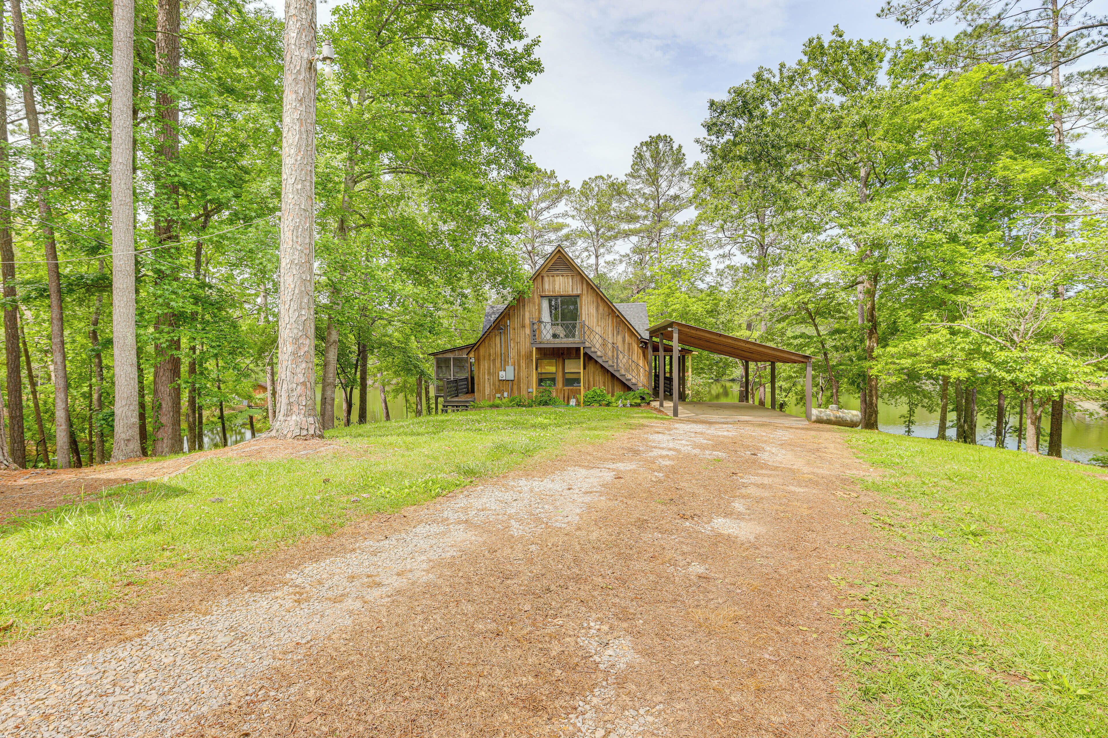 A rustic cabin with a porch, surrounded by tall trees and a gravel path leading to it.