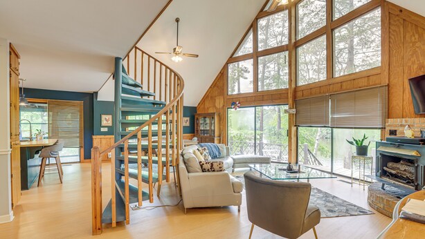 A spacious living area with a wooden staircase, a fireplace, and large windows offering a view of the outdoors. - Riverfront Shelby Home w/ Private Boat Dock! (Shelby)