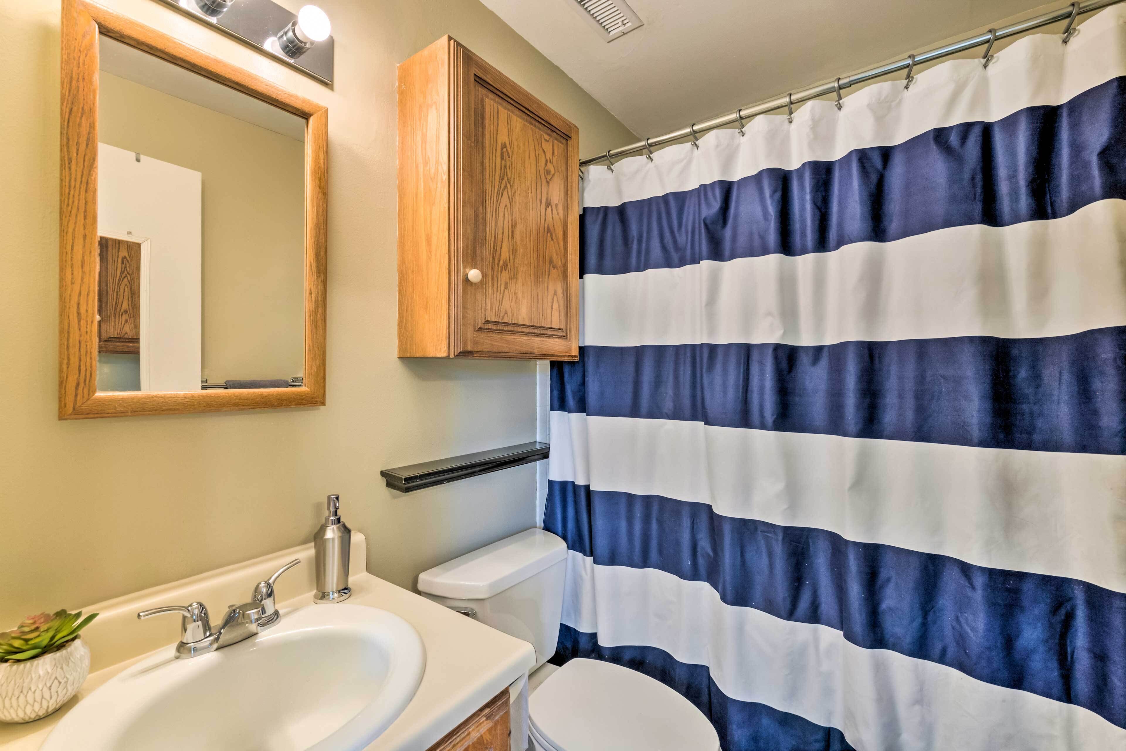 Un bagno con un lavandino bianco, uno specchio, un armadietto in legno e una tenda da doccia a righe.