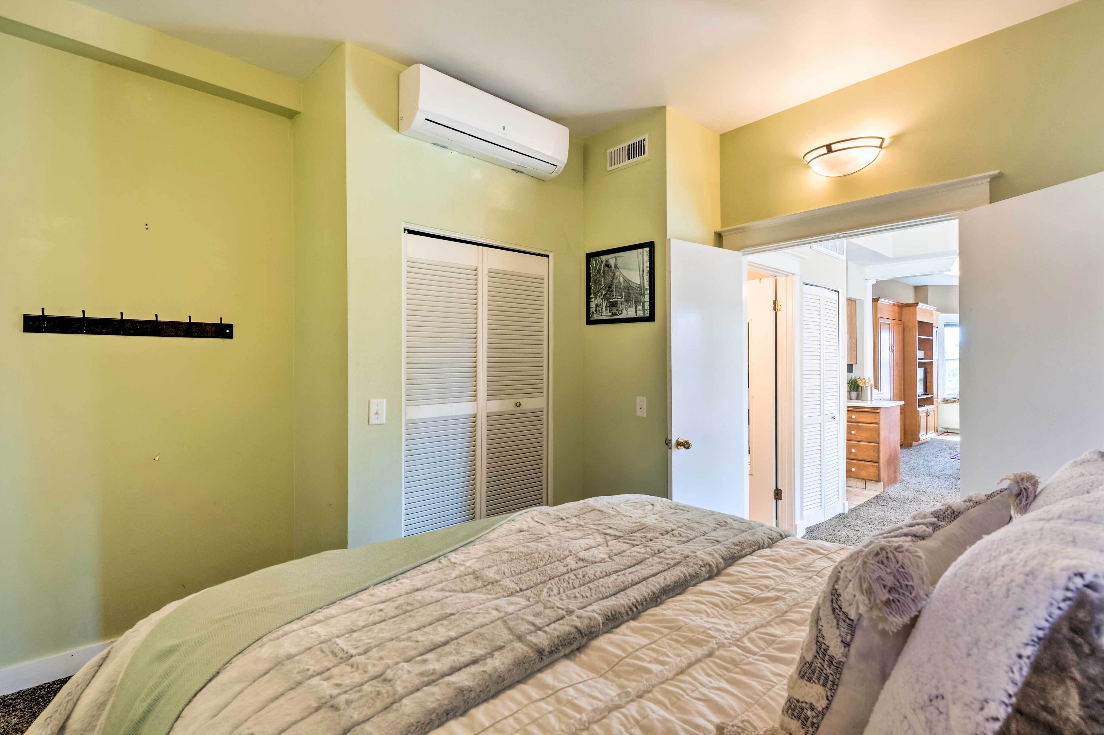 A bedroom with a bed, an air conditioner, a closet, and a hallway leading to a bathroom.