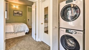 A laundry room with stacked washers and dryers, a bed with a white comforter, and a hallway leading to a bedroom. - Salt Lake City Condo < 28 Mi to Ski Resort! (Salt Lake City)
