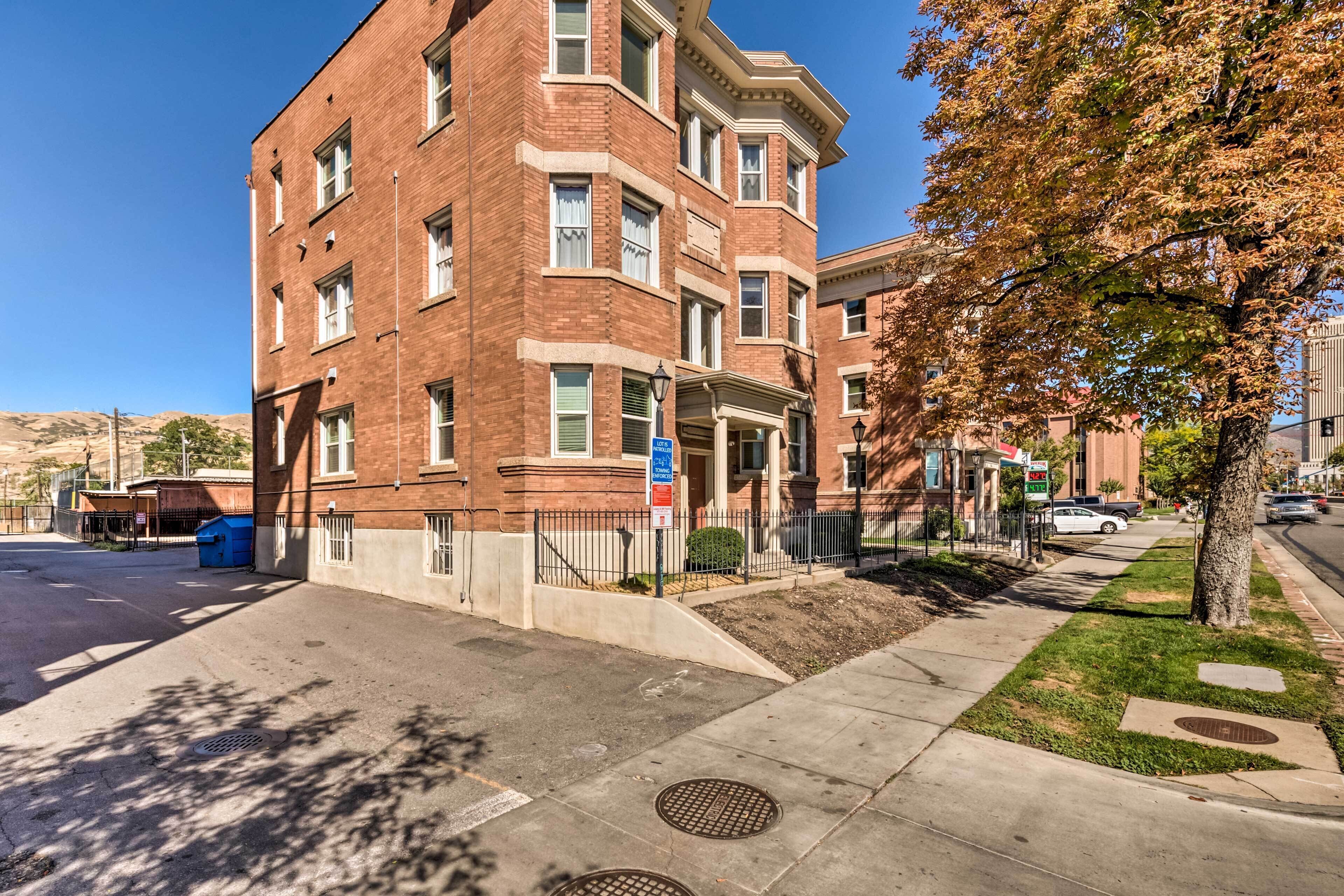 A multi-story brick building with a corner entrance, a sidewalk, a tree, and a street.