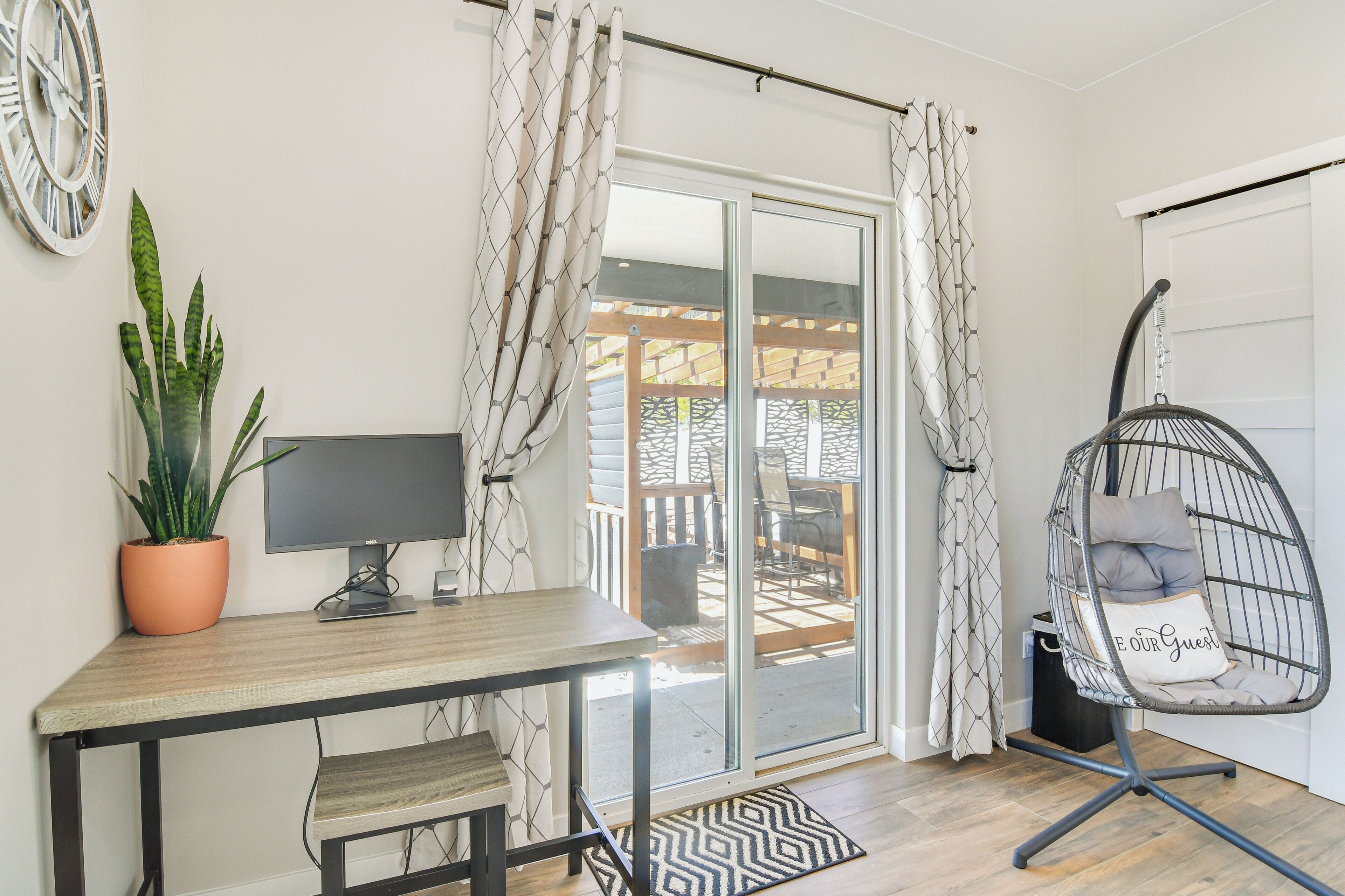 A modern room with a desk, computer, potted plant, and a hanging chair with a cushion.