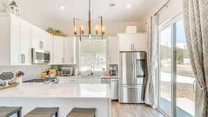 A modern kitchen with white cabinetry, a stainless steel refrigerator, and a large island with stools. - Romantic Mountain Retreat w/ Scenic Views! (Idaho Springs)