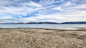 A barren landscape with a body of water and distant mountains under a cloudy sky.