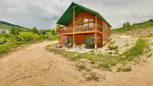 A two-story wooden cabin with a balcony, surrounded by a dirt path and greenery.