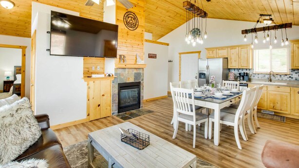 A modern kitchen with wooden cabinets, a large TV, and a dining area with white chairs and a table.