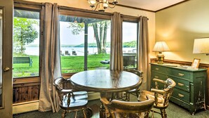Un espace repas comprenant une table ronde et des chaises, un lustre, et une vue sur un lac grâce à de grandes fenêtres.