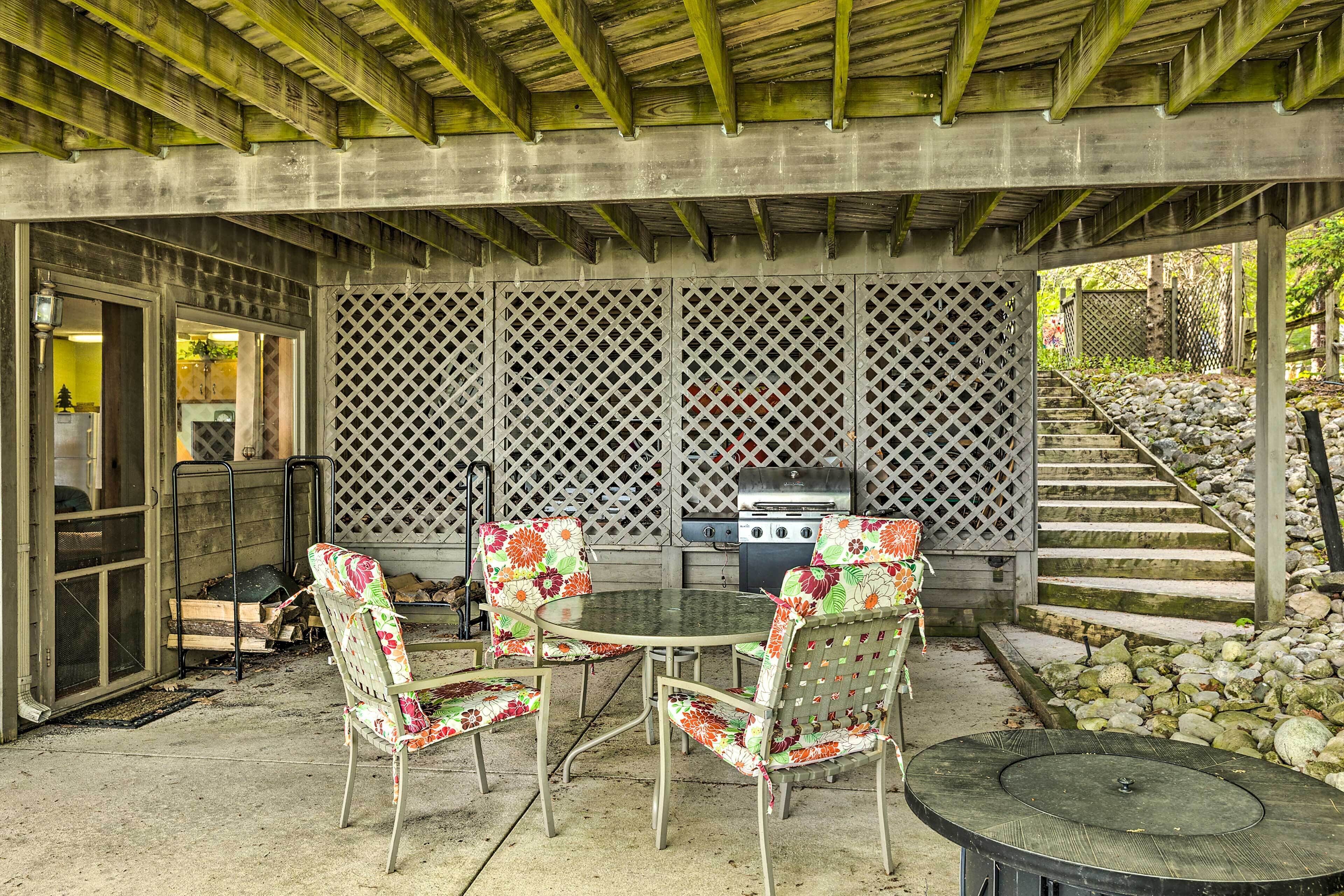 An outdoor patio with a round table and four chairs, a grill, and a wooden deck.