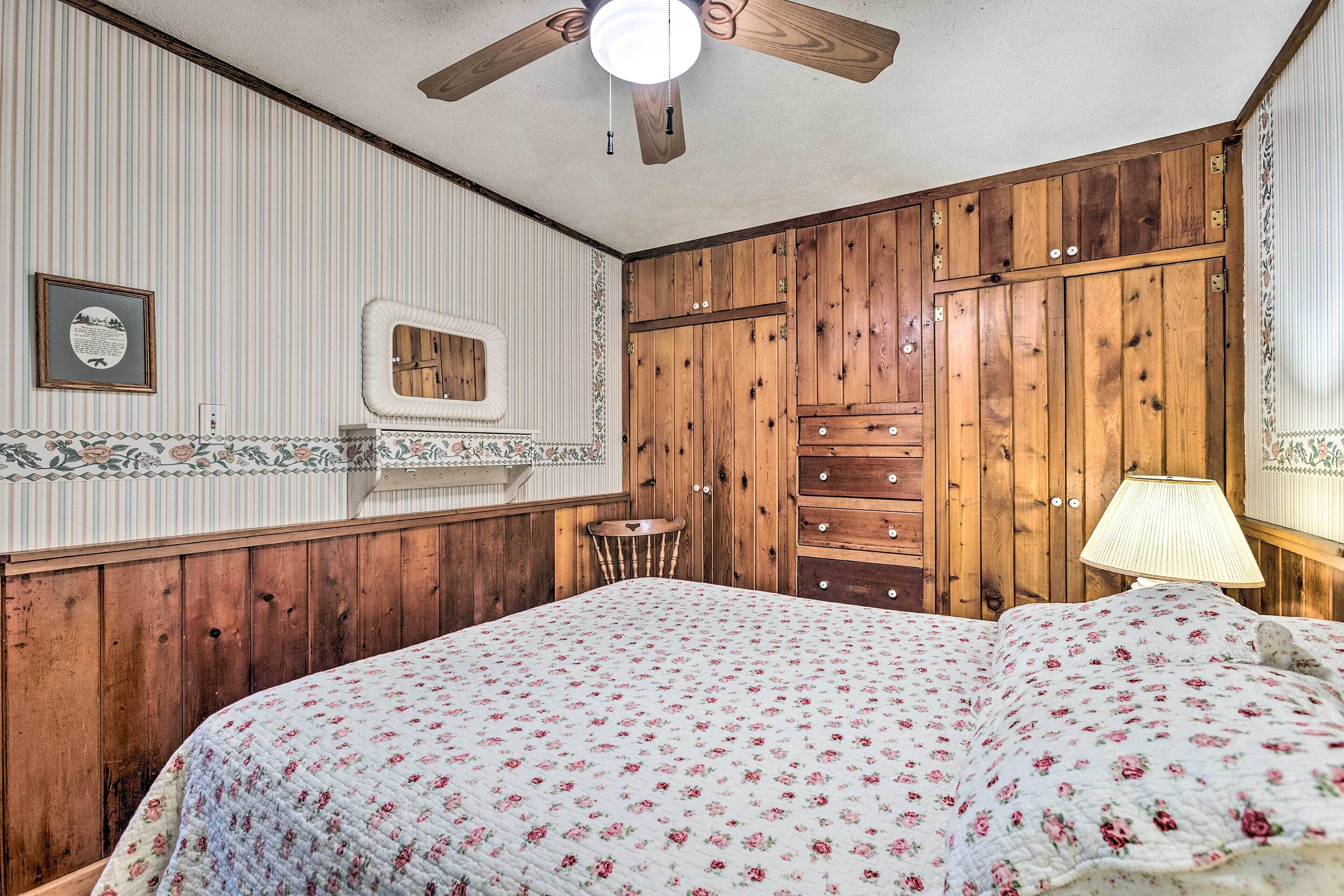 Ein Schlafzimmer mit einem Holzschrank, einem Bett mit floralem Überwurf, einem Deckenventilator und einem kleinen Nachttisch.