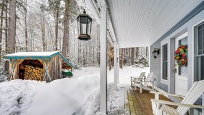 Ein mit Schnee bedeckter Winterbalkon mit weißen Adirondack-Stühlen und ein Holzschuppen mit blauem Dach.