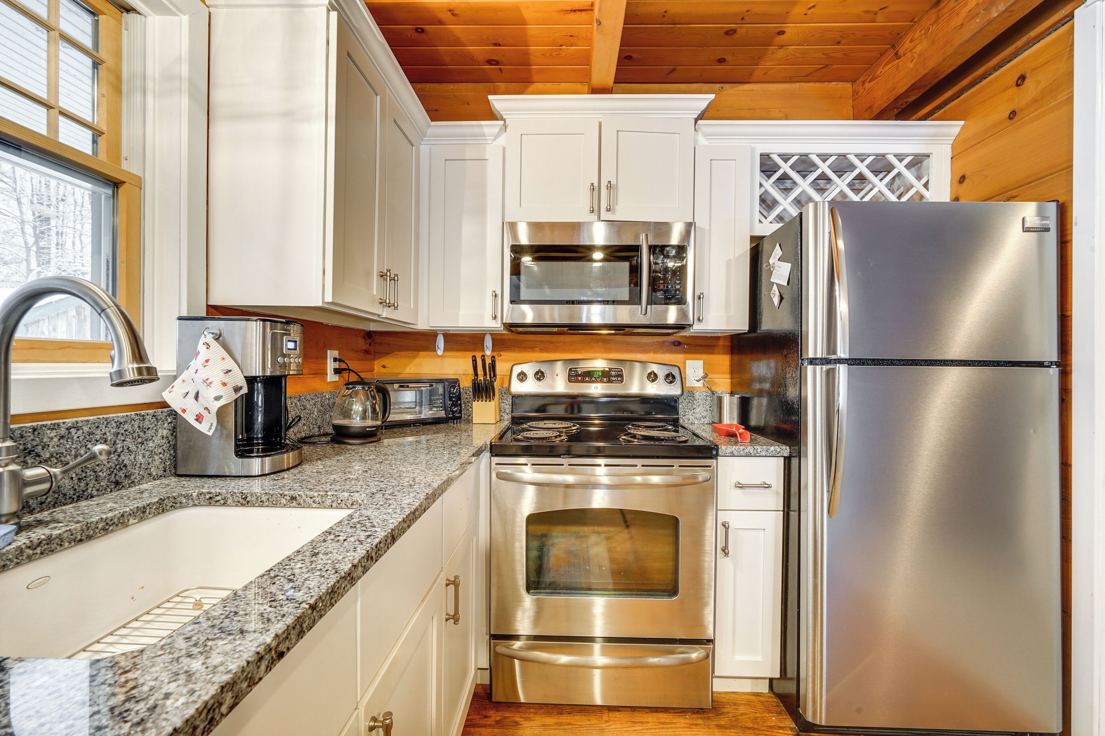 A modern kitchen with stainless steel appliances, white cabinets, granite countertops, and a wooden ceiling.