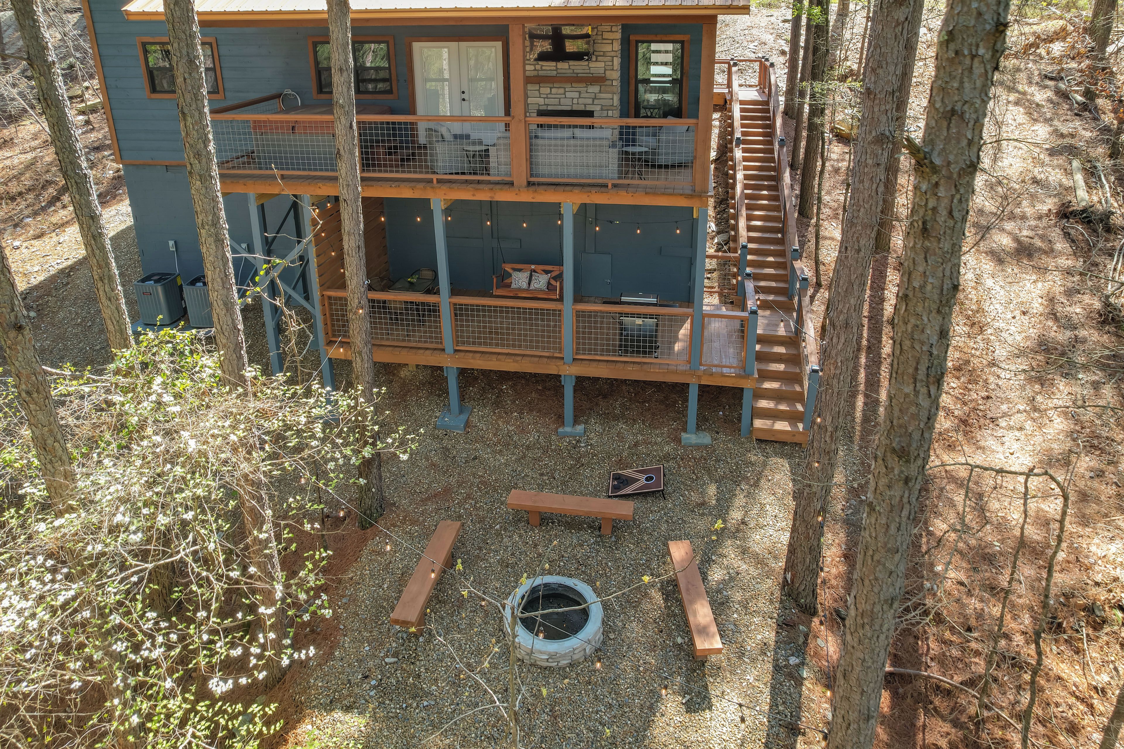 A multi-level wooden cabin with a fenced balcony area, surrounded by trees and a gravel ground.