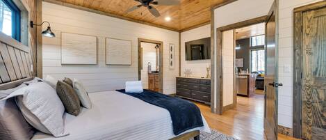 A bedroom with a wooden ceiling, a bed with a white and dark blue bedspread, a patterned rug, and a ceiling fan.