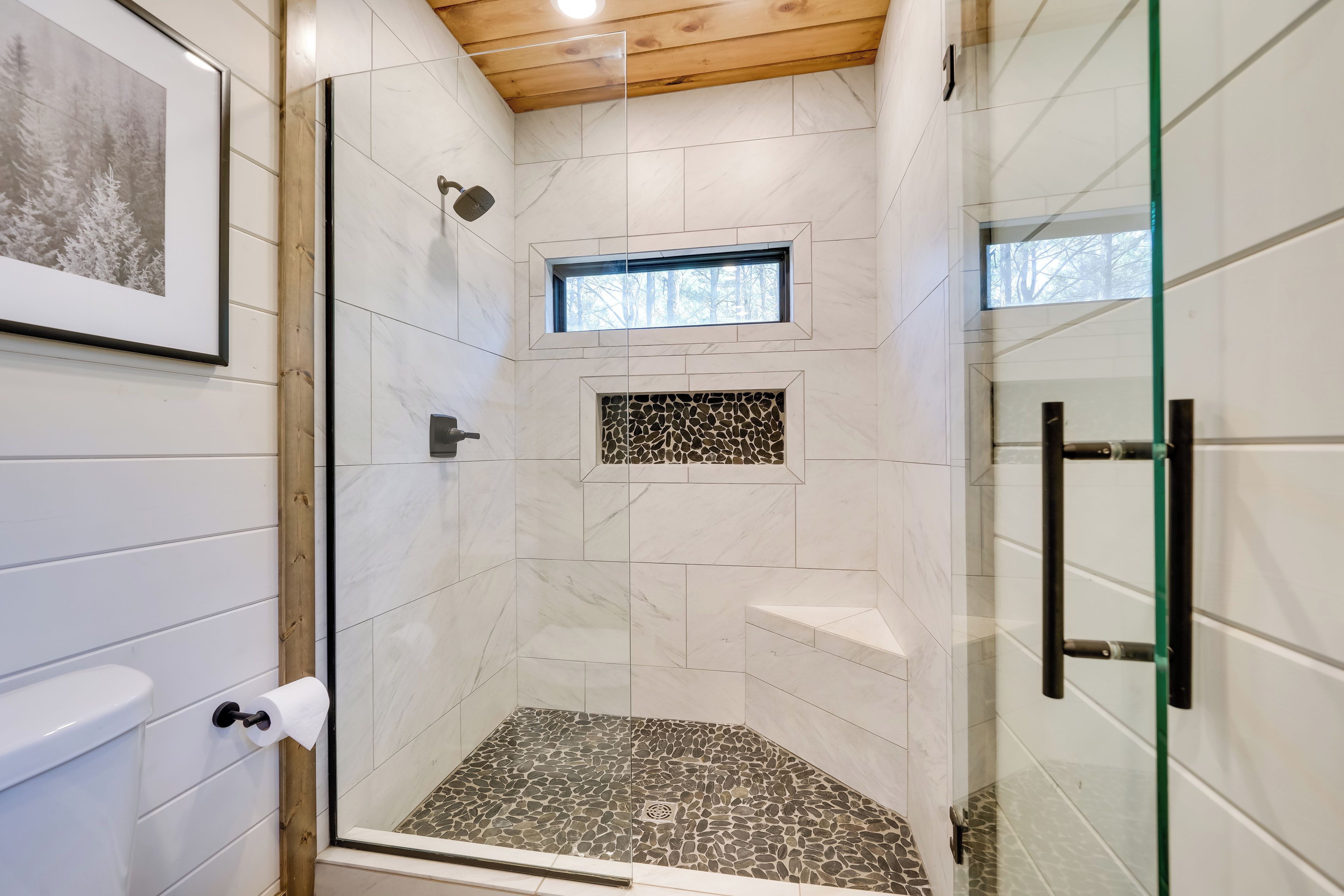 Ducha con puerta de vidrio, ventana pequeña y un reverso de mosaico de piedra.