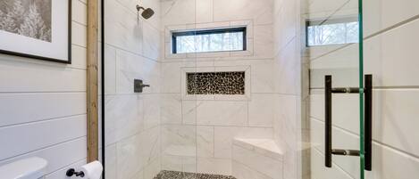 Ducha con puerta de vidrio, ventana pequeña y un reverso de mosaico de piedra.
