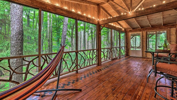 A wooden deck with a hammock, large windows, and a table with chairs. - Trails & Creek On-site: Tranquil Greentown Cabin (Greentown)