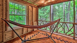 A hammock in a wooden cabin with large windows overlooking a forest. - Trails & Creek On-site: Tranquil Greentown Cabin (Greentown)