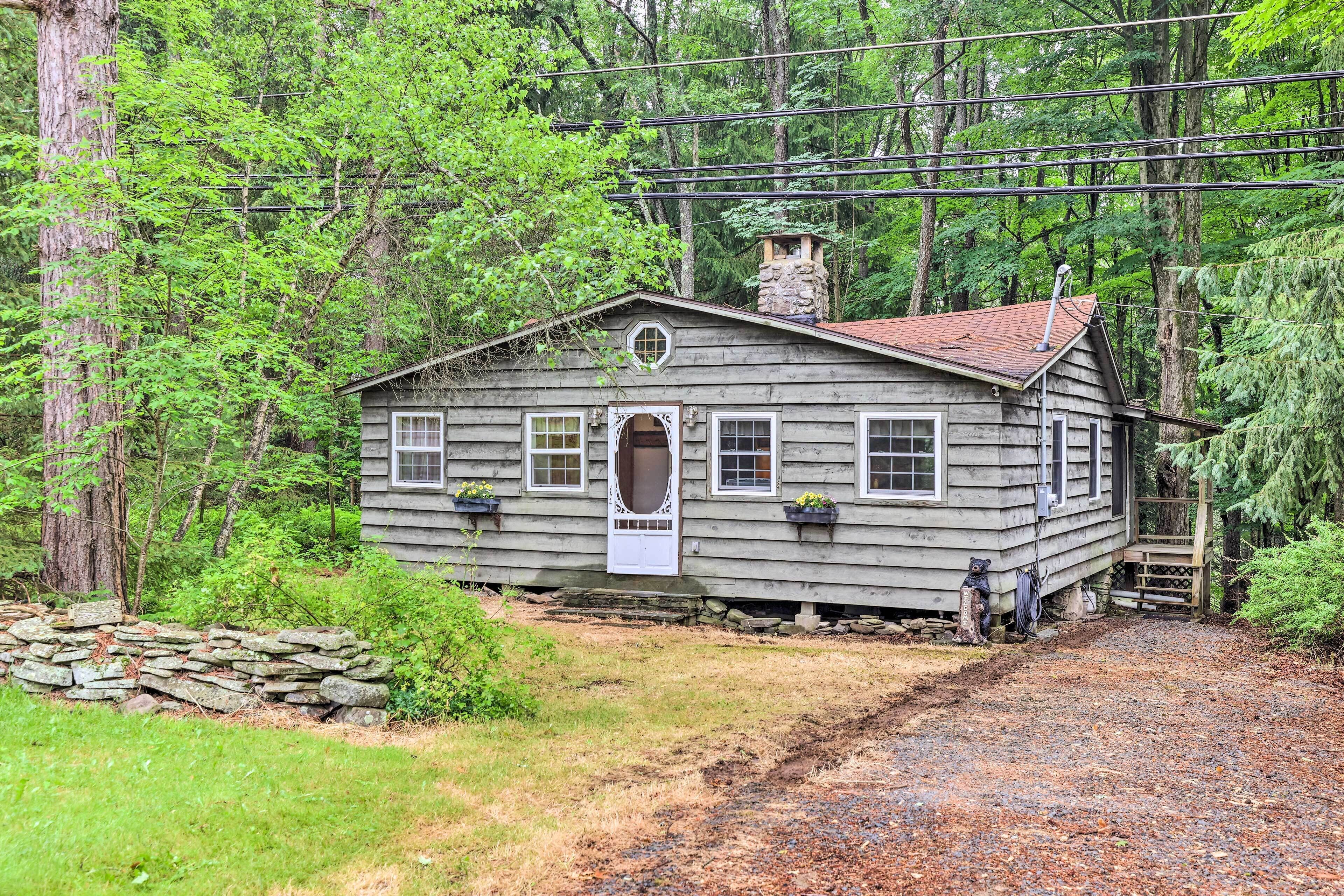A rustic cabin with a stone foundation, wooden siding, and a chimney.