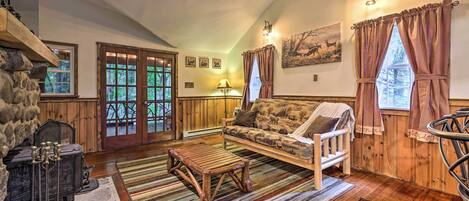 Een gezellige woonkamer met een stenen openhaard, houten meubels en een groot raam met gordijnen.