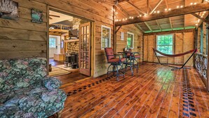 A wooden cabin interior with a hammock, floral sofa, and a dining area with chairs. - Trails & Creek On-site: Tranquil Greentown Cabin (Greentown)
