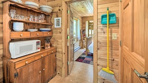 A wooden interior with a microwave, shelves with dishes, a broom, and a door with hooks. - Waterfront Escape w/ Fire Pit in Crosslake! (Pequot Lakes)