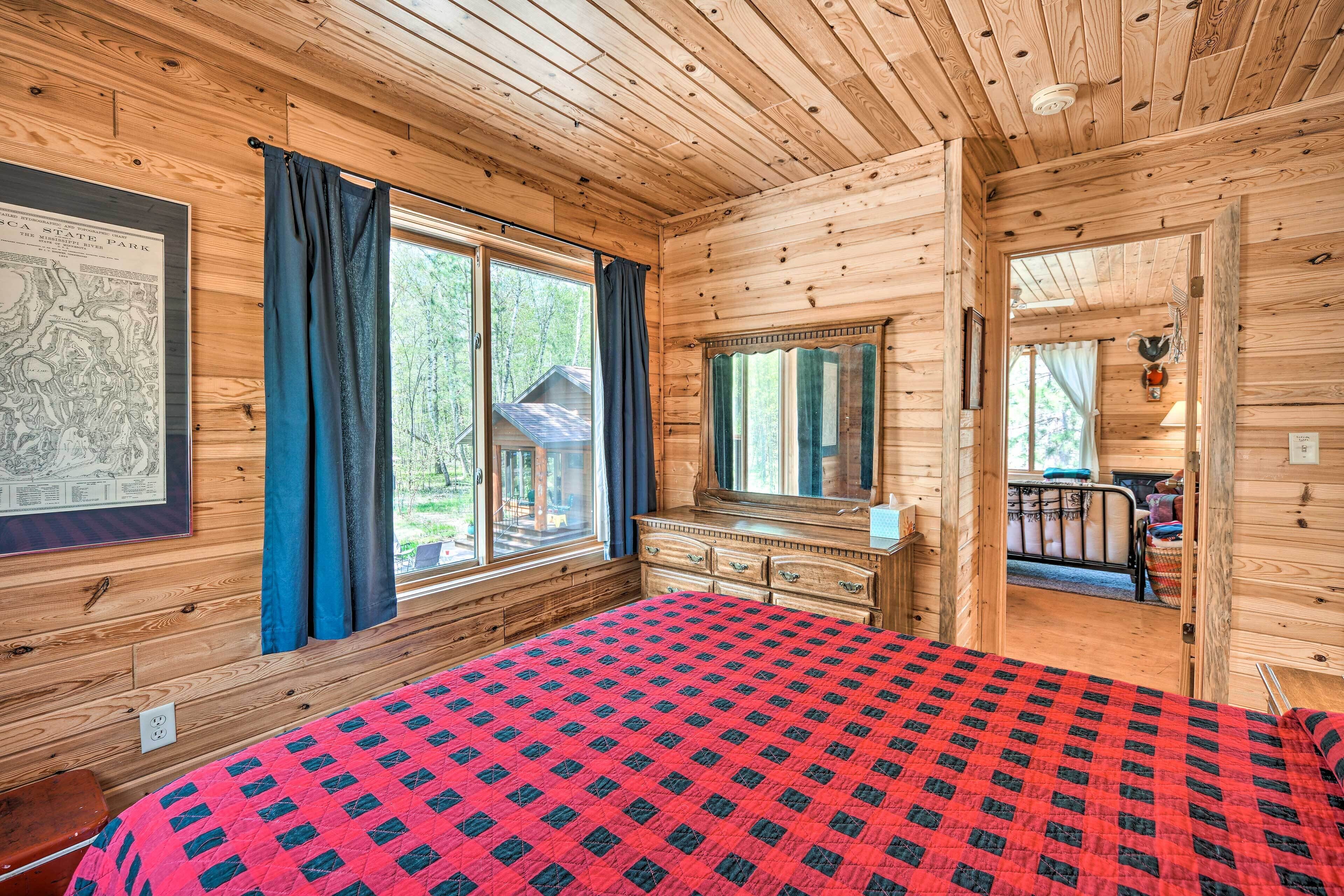 Ein Schlafzimmer einer Holzhütte mit Bett, Schminktisch und großen Fenstern.