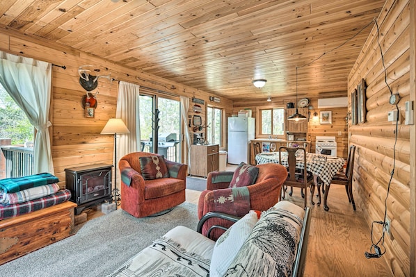A cozy cabin interior with a fireplace, wooden walls, a dining area, and a living room with a sofa and chairs.
