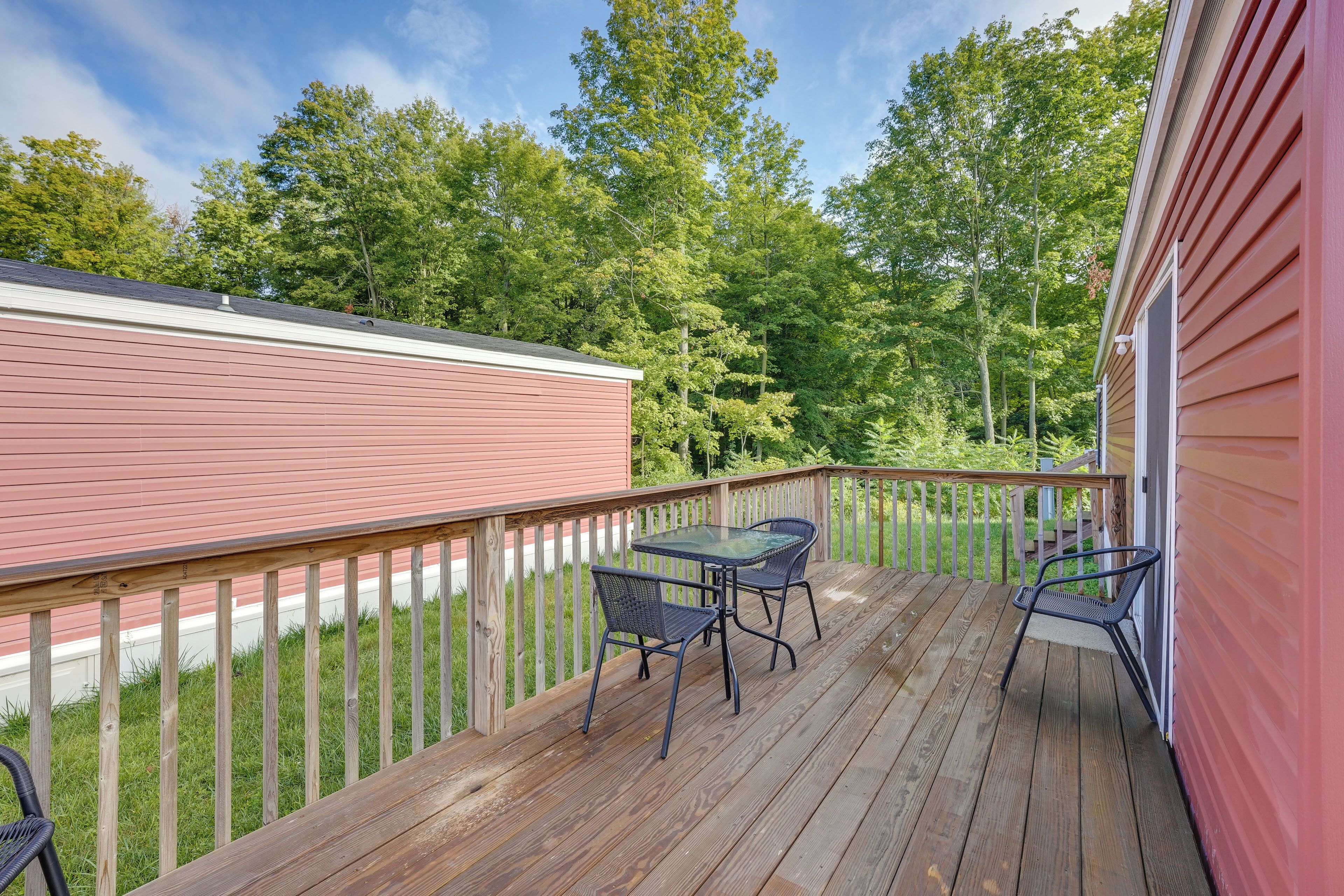 A wooden deck with a glass table and two chairs, surrounded by a wooden railing.