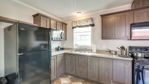 A kitchen with wooden cabinets, a black refrigerator, a sink, and a stove. - Cozy Cassopolis Cabin, Near Parks & Golfing! (Cassopolis)
