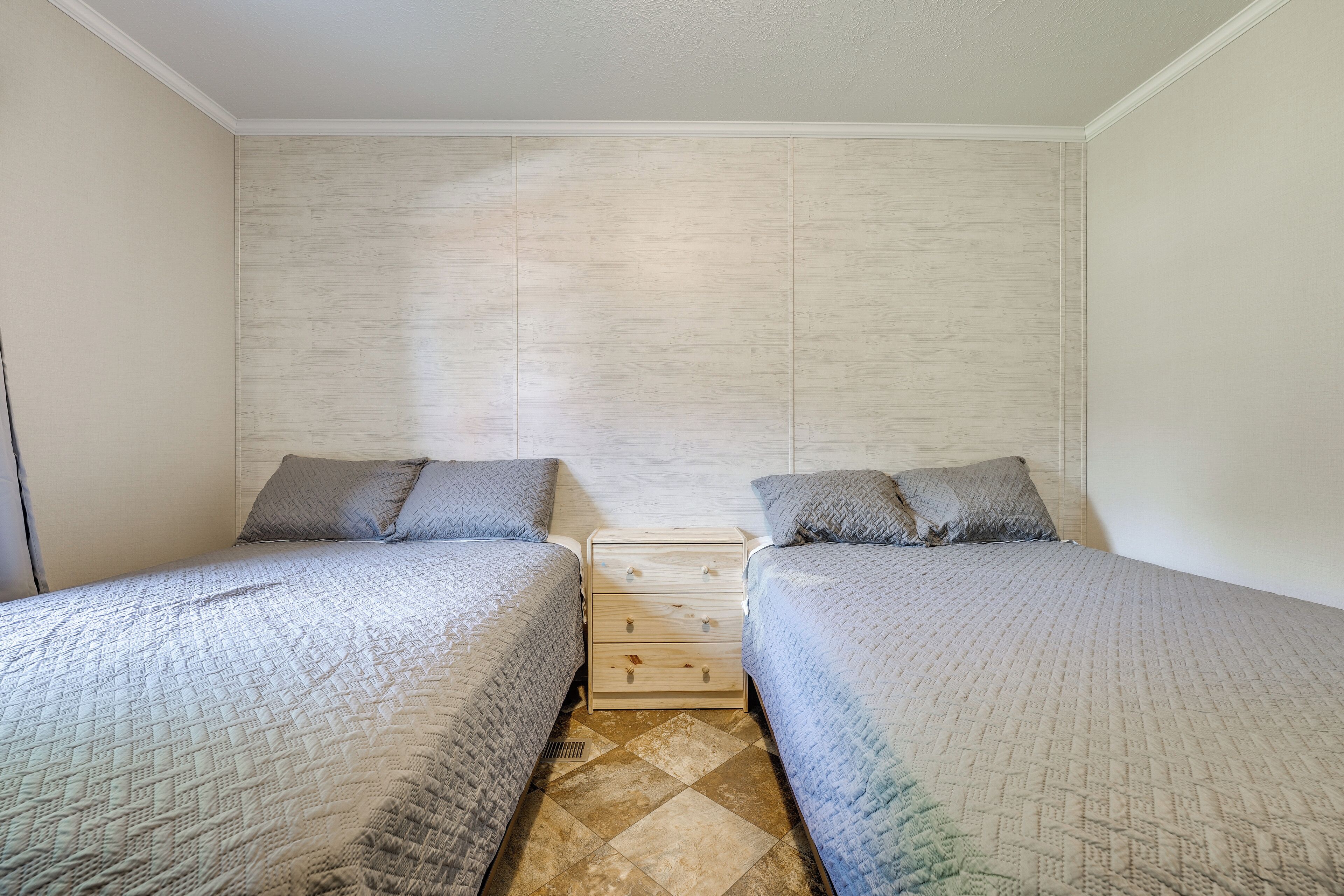 A bedroom with two single beds, a wooden nightstand, and a tiled floor.