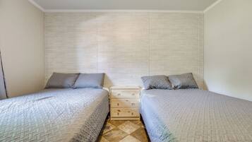 A bedroom with two single beds, a wooden nightstand, and a tiled floor.