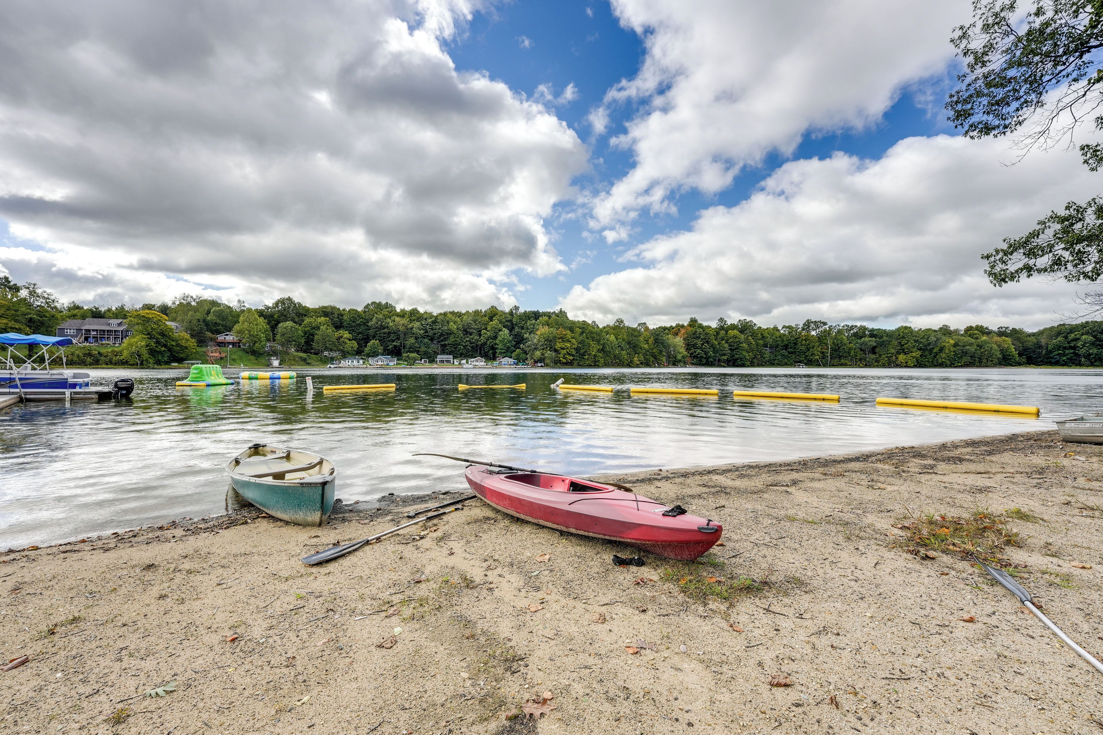 A lakeside view with boats, a sandy shore, and a forest in the background.
