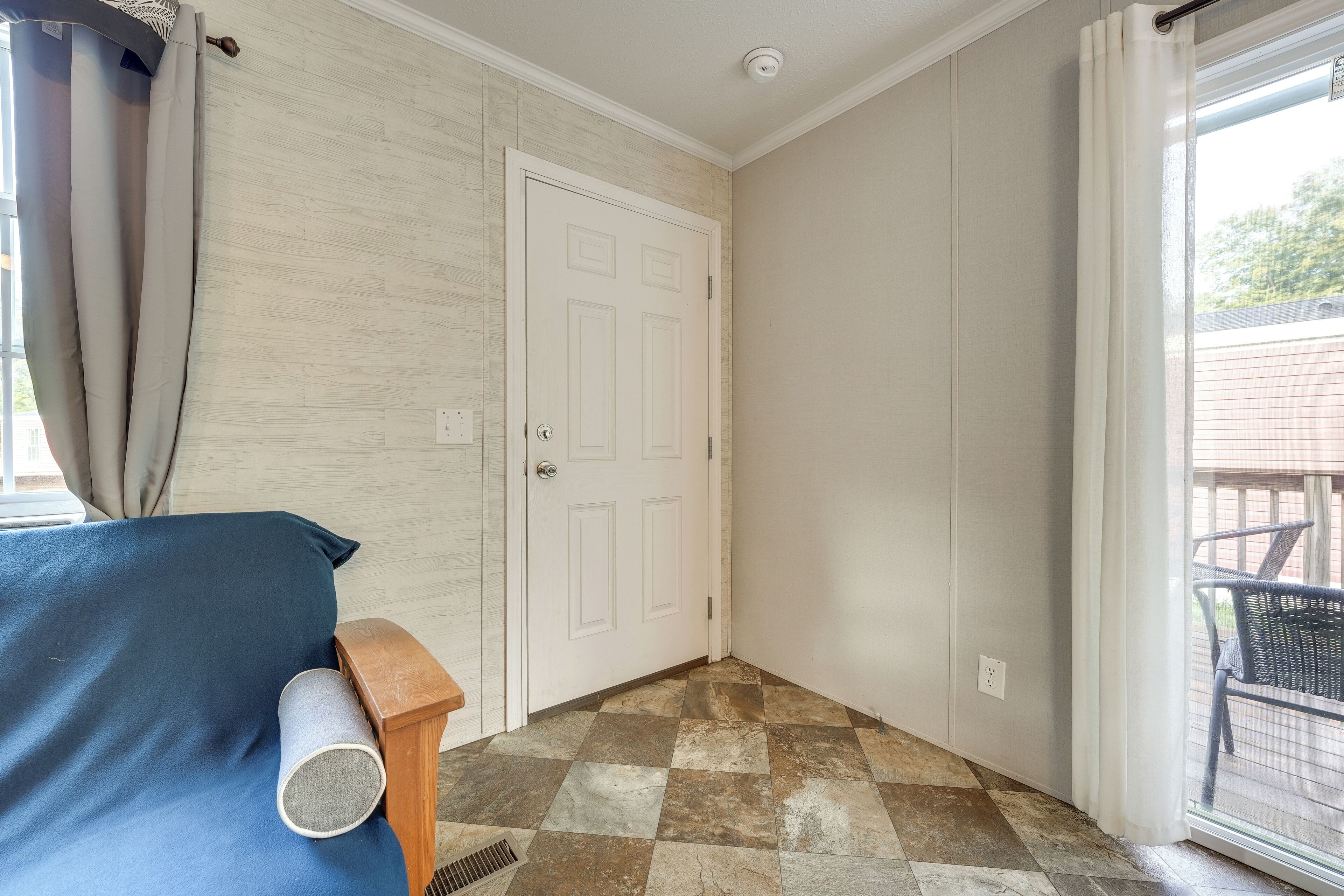 Una habitació amb un terra de petxines, una porta blanca i una finestra amb cortines.
