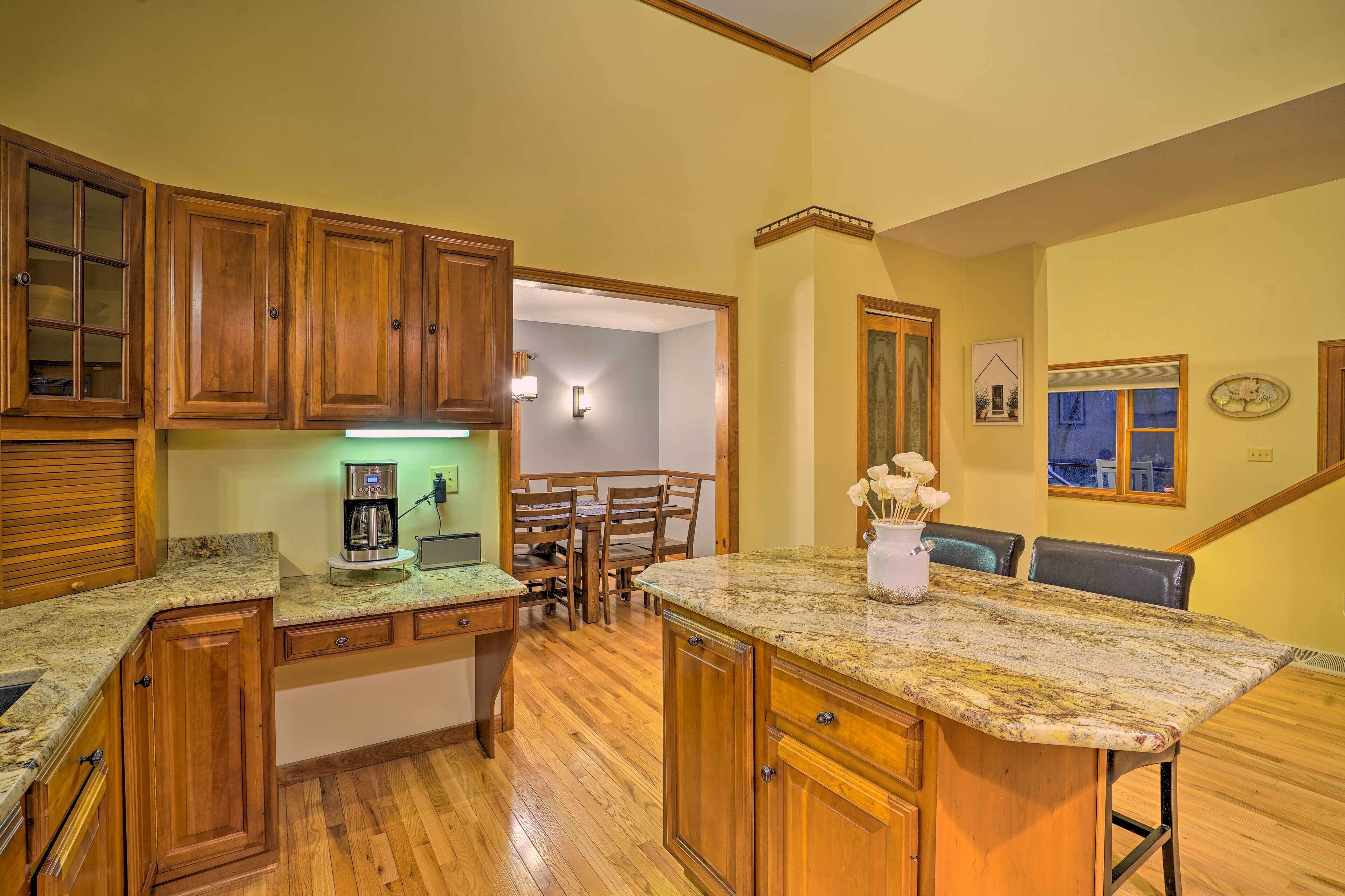 A kitchen with wooden cabinets, granite countertops, a coffee maker, and a dining area with chairs and a table.