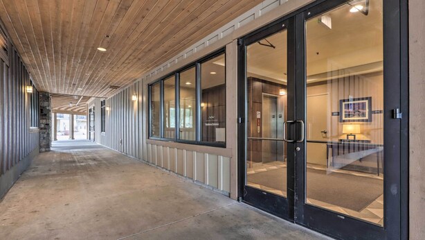 A corridor with a wooden ceiling, glass doors leading to an elevator, and a stone wall on one side. - Central Mccall Getaway: Walk to Payette Lake! (McCall)