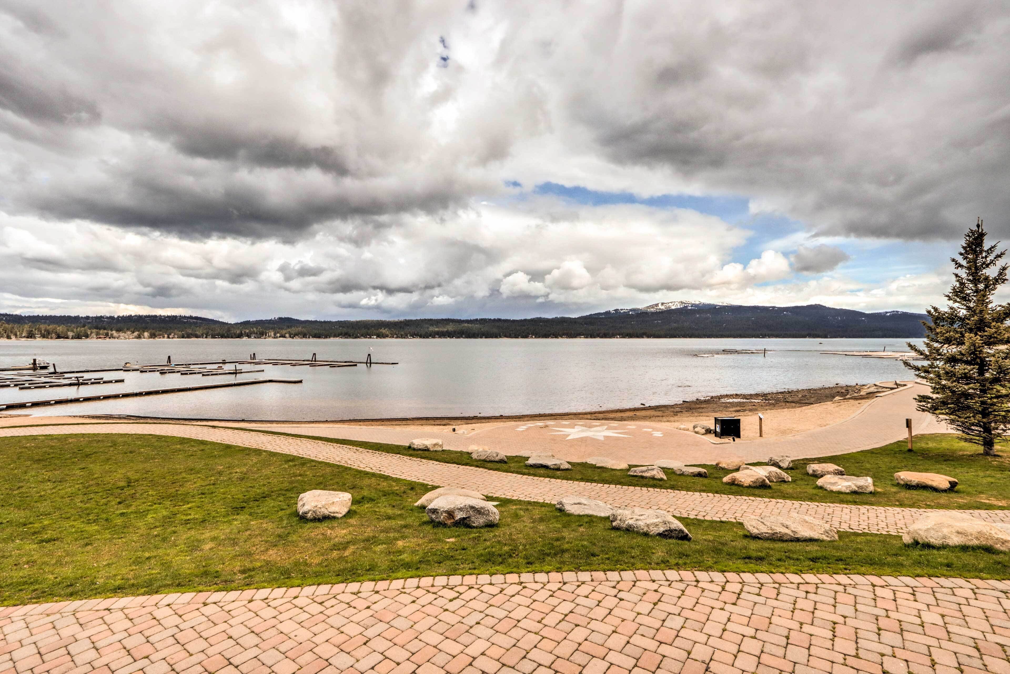 A lakeside park with a paved walkway, large rocks, and a dock extending into the water.